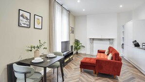A modern living room with a herringbone floor, a red sofa, a dining table with chairs, and a TV. - Host & Stay | Apartment 4, Upton House (Northampton)