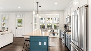 A modern kitchen with a central island, stainless steel appliances, and a view to an outdoor balcony. - Seabrook Glamping in the Woods | Hot Tub, Fire Pit, 3BR, Sleeps 9 (Pacific Beach)