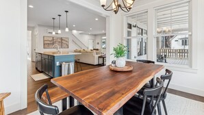 A spacious kitchen with a wooden dining table, modern pendant lights, and a view of the backyard through large windows. - Seabrook Glamping in the Woods | Hot Tub, Fire Pit, 3BR, Sleeps 9 (Pacific Beach)