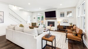 A spacious living room with a white sofa, a leather armchair, a fireplace, and a staircase. - Seabrook Glamping in the Woods | Hot Tub, Fire Pit, 3BR, Sleeps 9 (Pacific Beach)