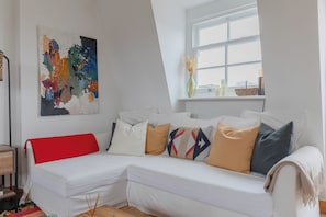 Un salon moderne avec un canapé d’angle blanc, un tableau abstrait aux couleurs vives et une vue par la fenêtre.