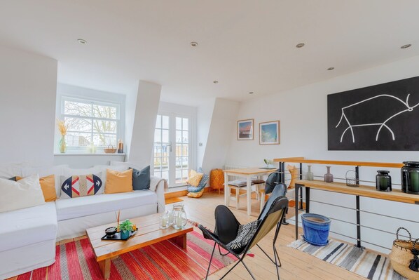 A spacious living room with a white sofa, a wooden coffee table, and a dining area with a wooden table and chairs.