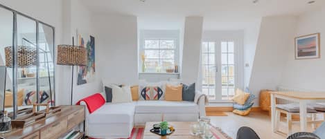 Un salon moderne avec un canapé blanc, une table basse en bois et un coin repas comprenant une table et des chaises blanches.