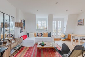 A modern living room with a white sofa, a wooden coffee table, and a dining area with a white table and chairs. - Perfect 2BD Duplex with Private Balcony, Islington (Greater London)