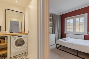 A bedroom with a bed, a washing machine, a dresser, and a window with curtains. - Perfect 2BD Duplex with Private Balcony, Islington (Greater London)