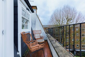 A balcony with wicker chairs and a small table, overlooking a residential area with buildings and bare trees.