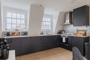 A modern kitchen with dark cabinets, a large window, and a view of the city. - Perfect 2BD Duplex with Private Balcony, Islington (Greater London)