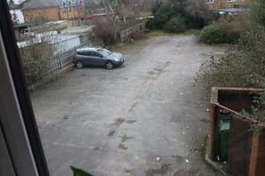 Ein Parkplatz mit einem in der Mitte stehenden Auto, umgeben von einer Hecke und Bepflanzung.