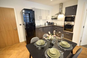 A modern kitchen with a dining table set for four, a refrigerator, microwave, oven, and a sink.