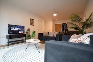 A modern living room with a flat-screen TV, a round coffee table, a sofa, and a potted plant.