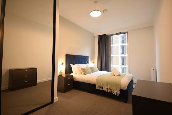 A bedroom with a bed, bedside tables, a dresser, a mirror, and a window.