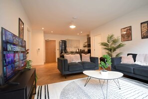 A living room with a sofa, coffee table, and a TV. There is a kitchen in the background. - Suite Life 2: 2-Bed, 2-Bath in New Cross (Greater Manchester)
