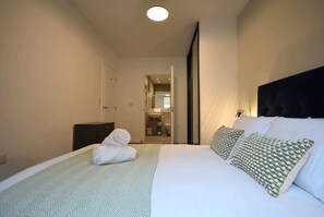 A hotel room with a bed, a bathroom visible through an open door, and a headboard with decorative pillows.