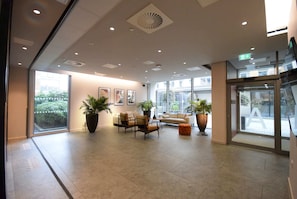 Un hall d’entrée spacieux, doté d’un canapé, de fauteuils, de plantes en pot et d’une grande porte vitrée donnant sur l’extérieur.