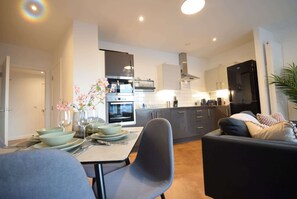 A modern kitchen with a dining area, a sofa, and a plant.