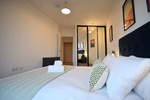 A hotel room with a large bed, a bedside table, a mirror, and a door leading to a bathroom. - Suite Life: 2-Bed, 1-Bath Top-Floor in New Cross (Greater Manchester)