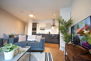 A modern living room with a sofa, coffee table, and TV. A kitchen is visible in the background.