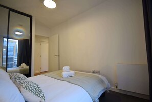 A hotel room with a large bed, a mirror, a door, and a view of a building outside.