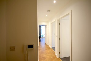 A hallway with a white wall, a ceiling light, and a door at the end.
