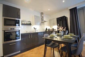 A modern kitchen with dark cabinetry, stainless steel appliances, and a dining area with a table set for four.