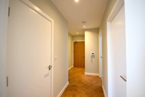 Un couloir aux murs blancs, au plancher en bois et aux portes blanches.