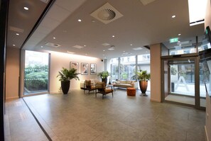 Eine geräumige Lobby mit einer Couch, Sesseln, Topfpflanzen und einer großen Glasdoor, die nach draußen führt.