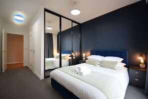 Une chambre d’hôtel moderne avec un grand lit, une armoire, un miroir et des lampes de chevet.