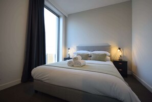 Ein Hotelzimmer mit einem großen Bett, einem Nachttisch mit zwei Lampen und einem Fenster mit Vorhängen.