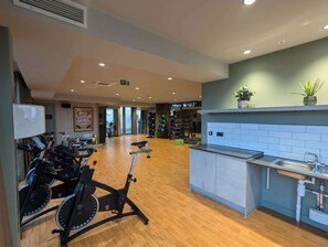 A gym with stationary bikes, a reception desk, and a wall-mounted plant.