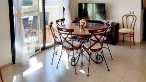 Een eetgedeelte met een ronde tafel, zes stoelen, een televisie en een fauteuil met kussen.