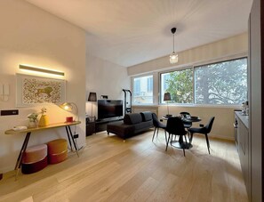 Un salon moderne doté d’un téléviseur à écran plat, d’un canapé, d’une table à manger avec des chaises et d’une grande fenêtre donnant sur la verdure.
