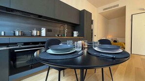 Una cuina moderna amb els armaris de color fosc, forn integrat i zona de menjador amb una taula rodona preparada per a dues persones.