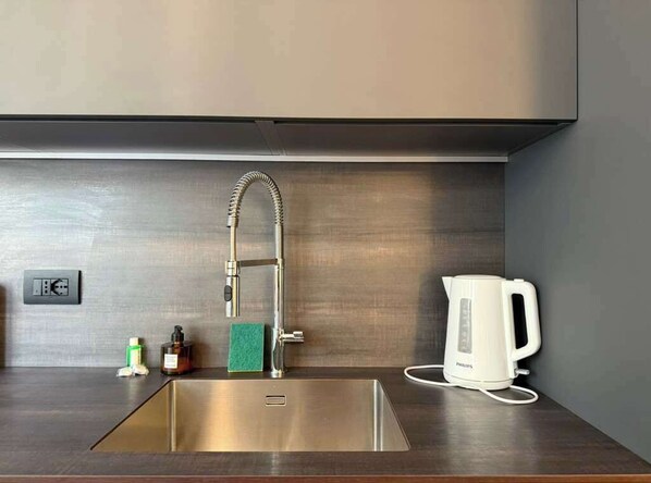 Une cuisine moderne équipée d’un évier en acier inoxydable, d’une bouilloire et d’un distributeur de savon.