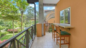 Un balcon avec une table et des chaises, donnant sur un jardin luxuriant agrémenté de palmiers et de plantes tropicales.