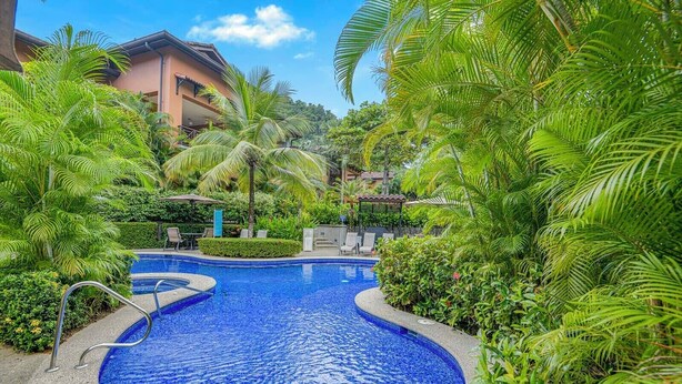 Une piscine entourée d’une végétation luxuriante et de palmiers, avec un bâtiment en arrière-plan.