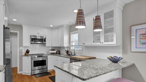 A modern kitchen with white cabinets, stainless steel appliances, granite countertops, and pendant lighting. - Seasaw Cottage - 5 bedroom pet friendly home on Wrightsville Beach (Wrightsville Beach)