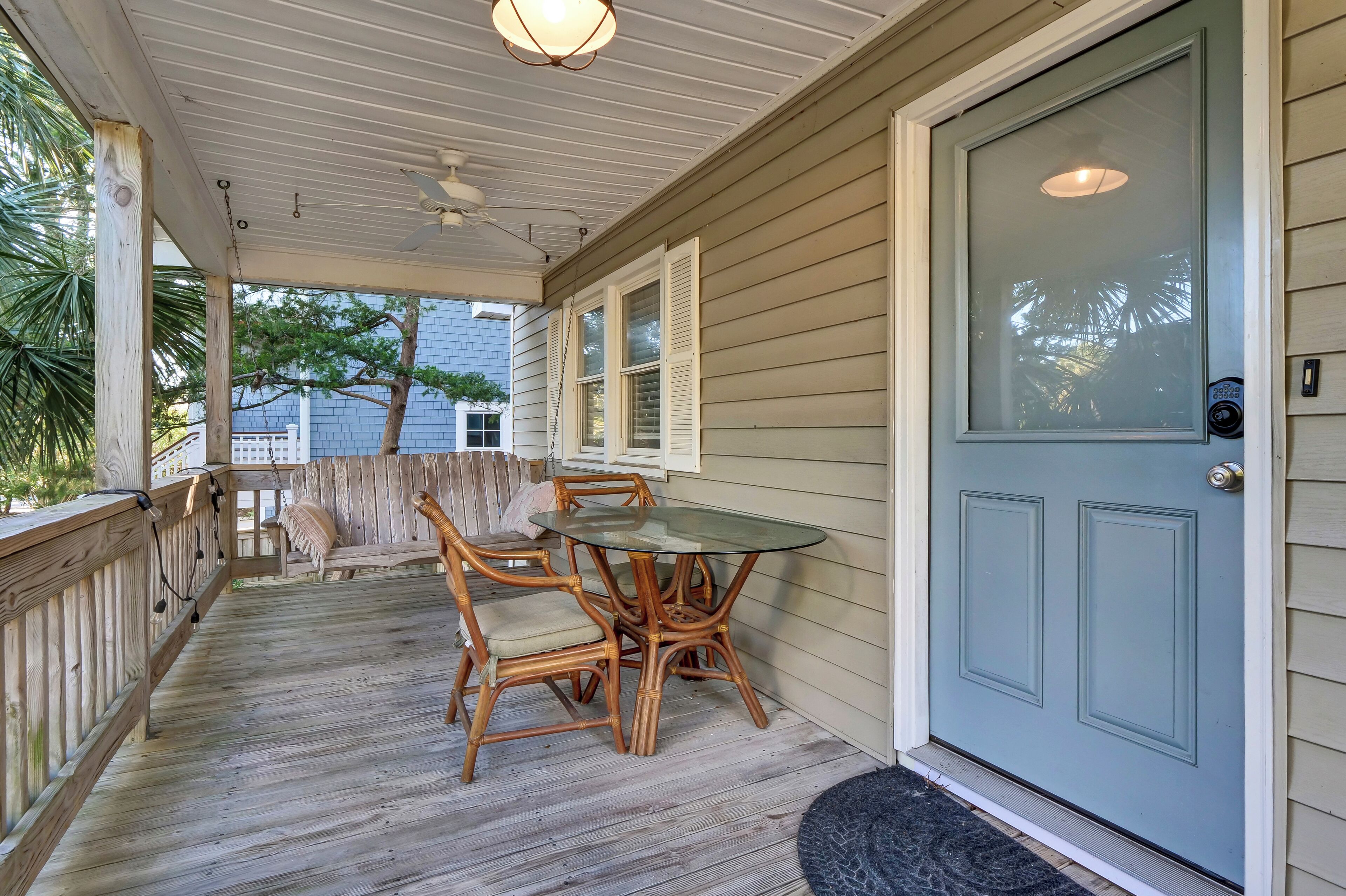 A covered porch with a glass table and wicker chairs, a wooden railing, and a blue door.