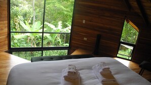 A room with a large window offering a view of lush greenery. There is a bed with neatly folded white towels. - Mogambo Ecolodge, a Private Botanical Garden Stay near Bogota (Bogotá)