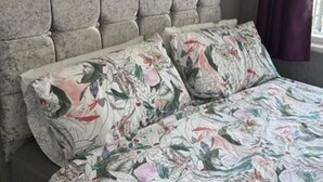 Un lit avec une literie à motifs floraux et une tête de lit capitonnée, dans une pièce dont les murs sont recouverts d’un papier peint à motifs.