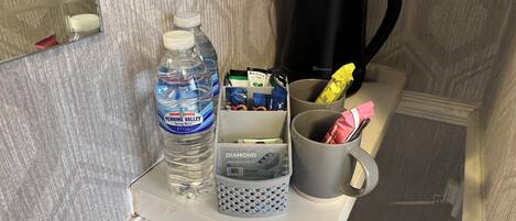 A small shelf with a water bottle, a coffee maker, a mug, and a box of tissues.