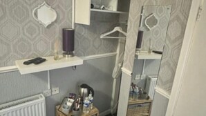 Une petite pièce avec un téléviseur fixé au mur, un radiateur, un petit meuble en bois et une poubelle.