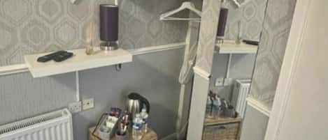 A compact room with a television mounted on the wall, a radiator, a small wooden cabinet, and a trash bin.