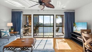 Un salon moderne doté d’un ventilateur de plafond, d’un téléviseur, d’un canapé, d’une table basse et d’un balcon offrant une vue sur l’océan.