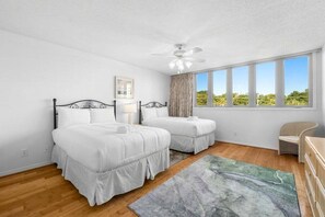 Ein Schlafzimmer mit zwei Betten, einem Deckenventilator, einem Fenster mit Blick ins Grüne und einem Sessel.