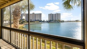 Une vue depuis un balcon, avec un palmier et une étendue d’eau en arrière-plan.
