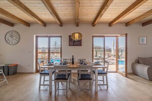 A dining area with a wooden table set for four, large windows, and a view of an outdoor pool. - Villa Malena in Svetvincenat (Svetvincenat)
