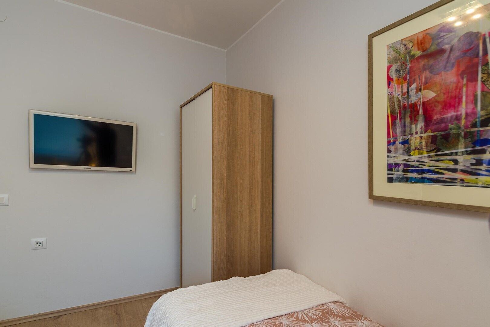 Quarto com cama, televisão, guarda-roupa e um quadro na parede.