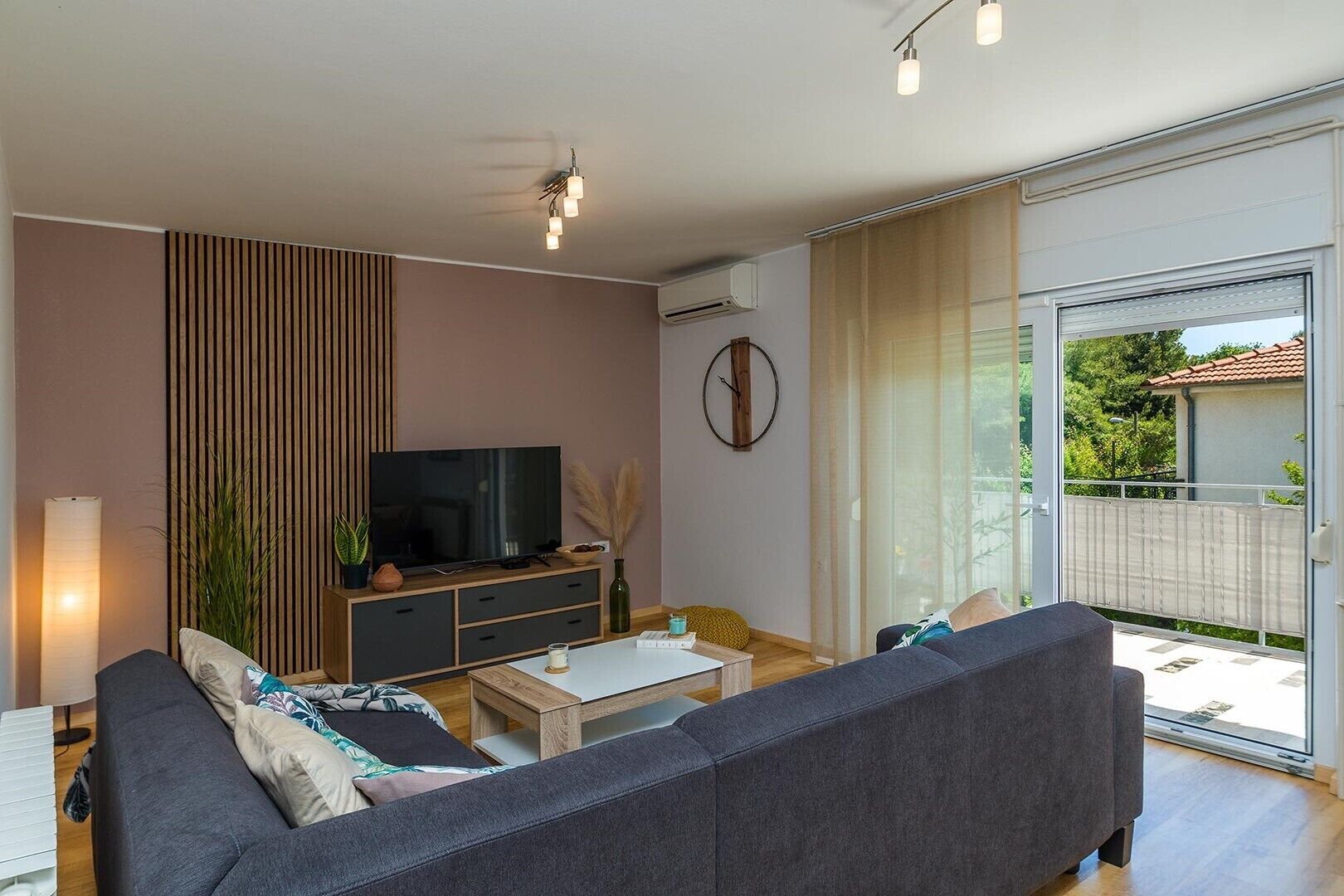 Een moderne woonkamer met een bank, televisie en een schuifdeur naar een balkon.
