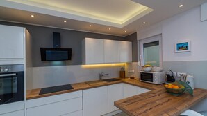 A modern kitchen with white cabinetry, a wooden countertop, and built-in appliances including an oven and microwave. - Beautiful Villa Suton with a Private Pool (Pula)