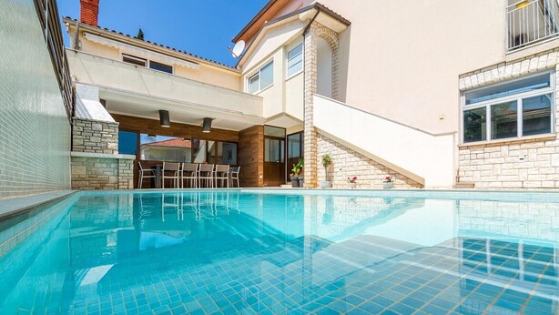 A swimming pool with tiled flooring, a covered seating area with chairs, and a stone wall. - Beautiful Villa Suton with a Private Pool (Pula)